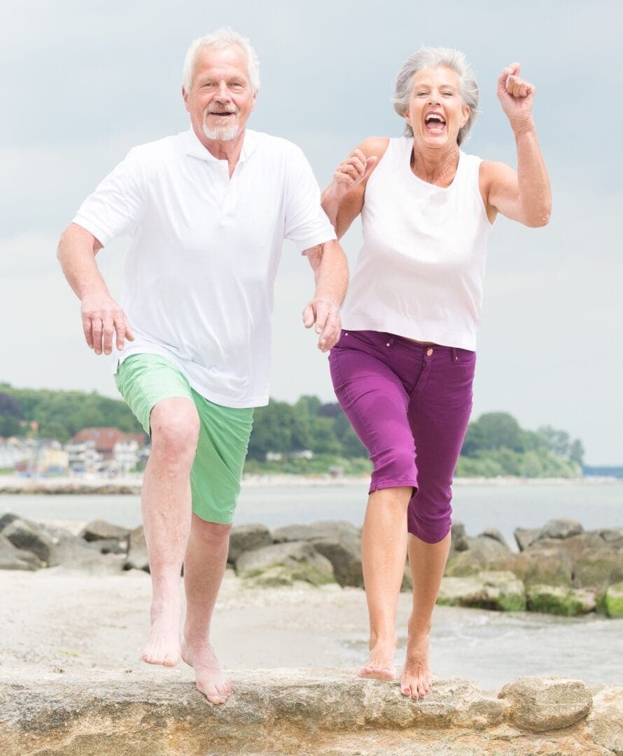 Smiling senior couple jogging along the shoreline on a sunny day. Healthy active lifestyle.