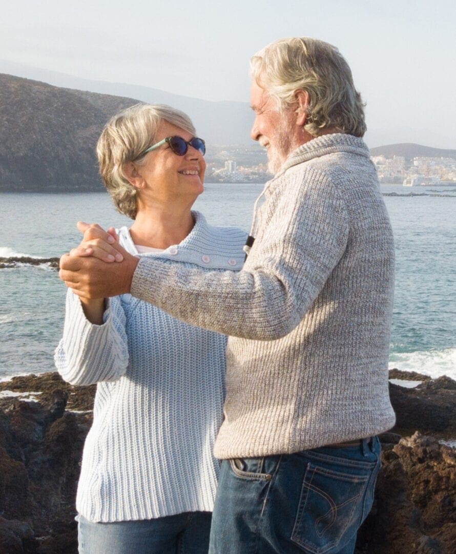 Smiling couple holding hands looking at each other in dance pose outside on a nice sunny day with background water mountain and town view. Healthy active lifestyle.