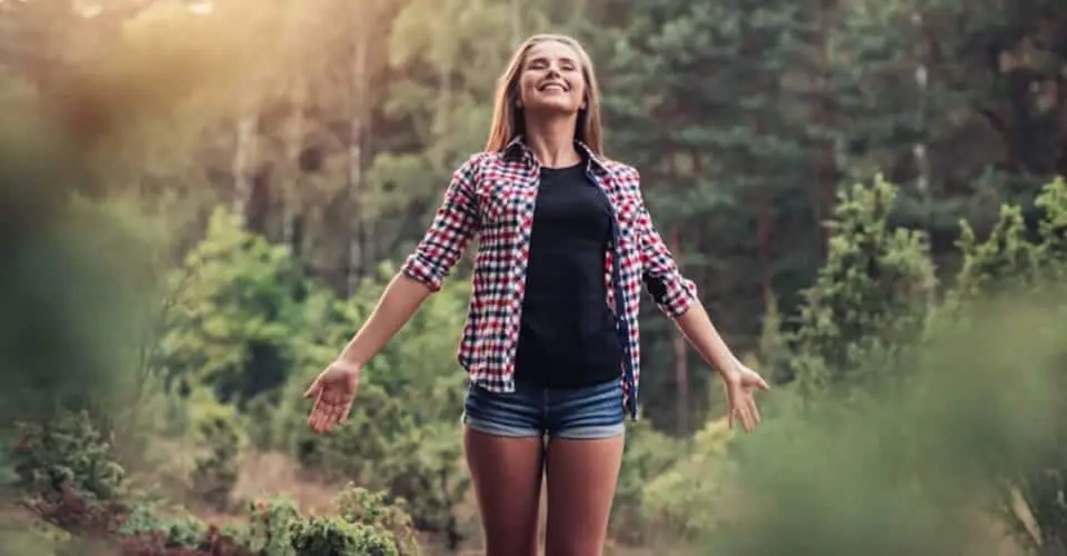 A woman in shorts and plaid shirt standing on top of a hill.