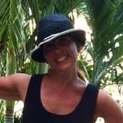 A woman in black shirt and hat near trees.